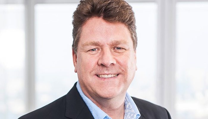 Professioneller Mann mit lächelndem Gesicht, im Anzug vor einem hellen, modernen Hintergrund.